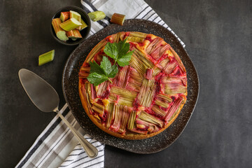 Freshly baked rhubarb pie, cut stalks and cake server on black table, flat lay