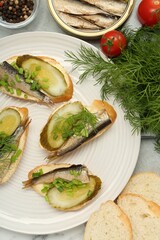 Delicious sandwiches with sprats, pickled cucumber, green onion and dill served on table, flat lay