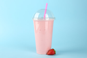 Plastic cup of tasty smoothie and fresh strawberry on light blue background