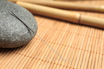 Acupuncture needle and spa stone on bamboo mat, closeup. Space for text