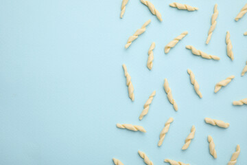 Uncooked trofie pasta on light blue background, flat lay. Space for text