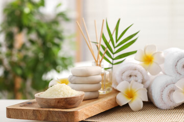 Composition with different spa products, plumeria flowers and palm leaves on table indoors, closeup