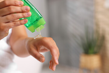 Young woman applying aloe gel onto her hand in bathroom, closeup. Space for text