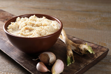 Spicy horseradish sauce in bowl, roots and garlic on wooden table, closeup