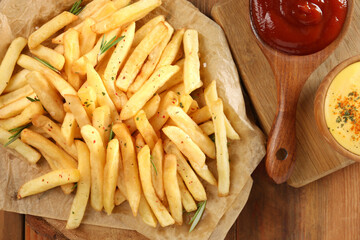 Delicious french fries served with sauces on wooden table, flat lay