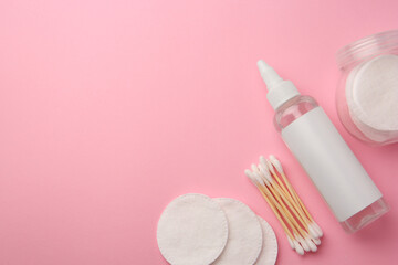 Bottle of makeup remover, cotton pads and swabs on pink background, flat lay. Space for text
