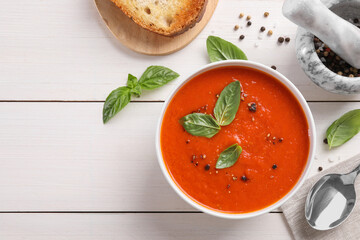 Flat lay composition with delicious tomato cream soup in bowl on white wooden table. Space for text