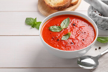 Delicious tomato cream soup in bowl on white wooden table, space for text