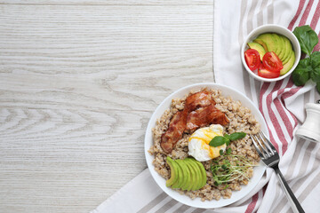 Delicious boiled oatmeal with poached egg, bacon and avocado served on light wooden table, flat lay. Space for text