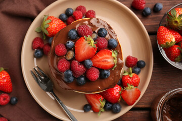 Stack of tasty pancakes with fresh berries and chocolate spread on wooden table, flat lay