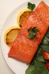 Tasty grilled salmon with basil, tomatoes and lemon on white wooden table, top view