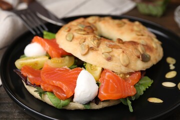 Tasty bagel with salmon, mozzarella cheese, tomatoes and lettuce on wooden table, closeup