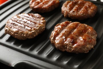 Delicious hamburger patties cooking on electric grill, closeup