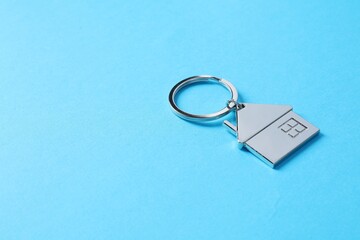Metallic keychain in shape of house on light blue background. Space for text