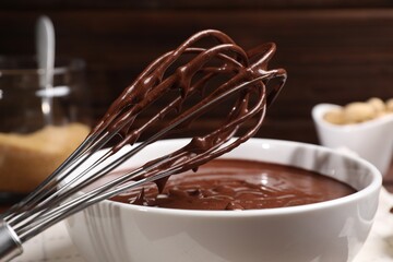 Bowl and whisk with chocolate cream on table, closeup
