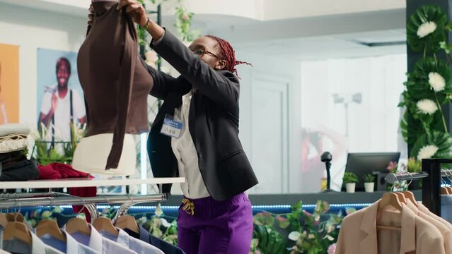 Woman restocking luxury fashion boutique elegant clothes on mannequin. African american worker replacing old collection with new season high class garments in trendy clothing store