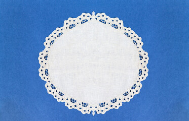 Round white table napkin with cutwork embroidered lace edge on a blue background. Blank space for...