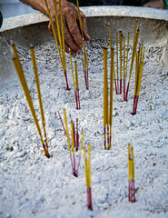 A hand of an older person placing, arranging standing sticks of incense in groups of 3 in a large...