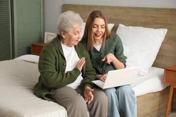 Young woman with her grandmother using laptop in bedroom