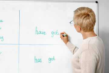 Female teacher writing English grammar on flipboard in classroom