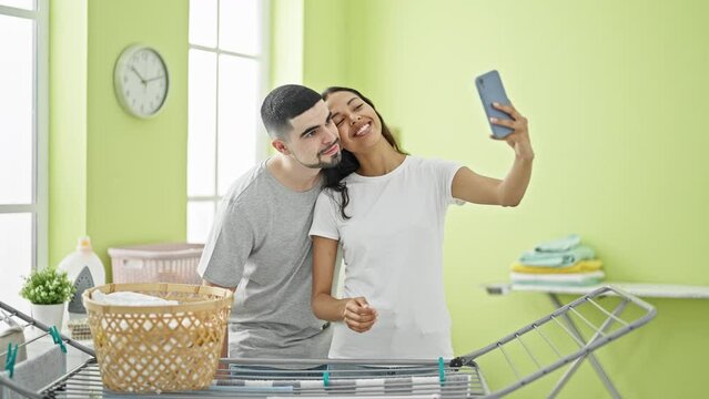 Smiling beautiful couple snapping a sweet laundry room selfie in amidst household chores, juxtaposed against clothes hanging on clothesline background