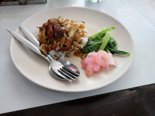 Roasted duck and crispy pork over rice with boiled bok choy and pink pickled ginger on a white...