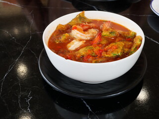 Deep fried egg with cha om leaves or Acacia omelets and fresh shrimp in sour curry soup in a white bowl, Asian traditional food style in Thailand