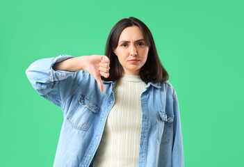 Young woman showing dislike on green background