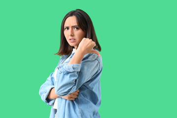 Upset young woman showing dislike on green background