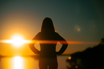 Silhouette of a Woman Looking at a River During Sunset. Girl admiring a peaceful landscape by the...