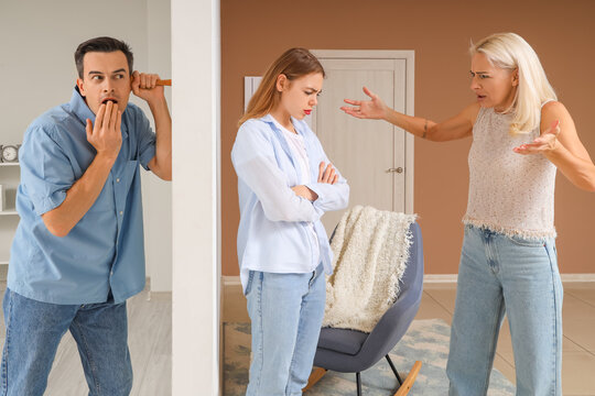 Young man eavesdropping on quarreling neighbours through wall in house