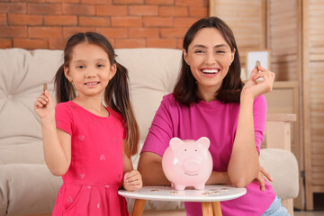 Little girl with her mother putting coins into piggy bank at home