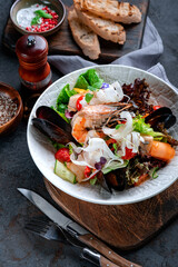 Fresh Salad with seafood, vegetables and herbs. Diet salad with shrimp, octopus, shellfish and fish in white plate on table