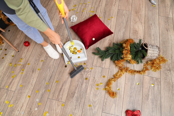 Female janitor sweeping floor in messy living room after New Year party