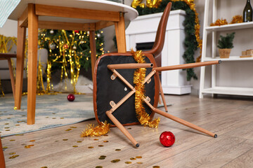 Fallen chair with tinsel in messy living room after New Year party
