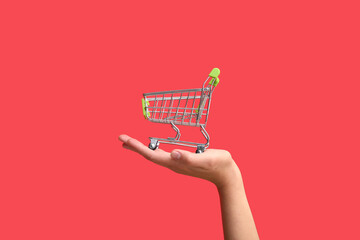 Female hand with green shopping cart on color background. © Pixel-Shot
