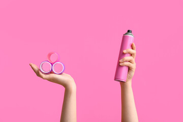 Female hands with hairspray and curlers on pink background.