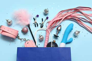 Shopping bag with different sex toys and Christmas decor on blue background