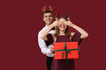 Beautiful young couple in reindeer horns with Christmas gift box on red background