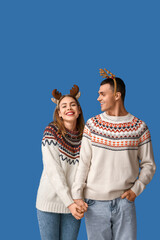 Happy young couple in reindeer horns on blue background