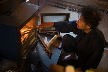 A man putting firewood into a wood stove Image of winter preparation in the countryside in a...