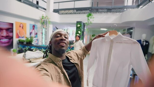 Man filming POV vlog while doing shopping in elegant fashion boutique, giving viewers info. Influencer doing social media content in clothing store, promoting clothing store new collection stock