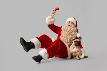 Happy Santa Claus with French bulldog and Christmas bell on grey background