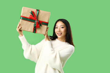 Young Asian woman with Christmas gift box on green background