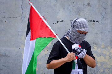 Man wearing a keffiyeh holds the Palestinian flag with hand on chest.