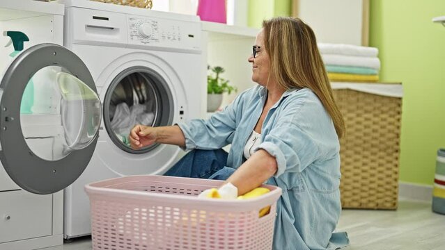 Middle age hispanic woman smiling confident washing clothes doing thumb up gesture at laundry room