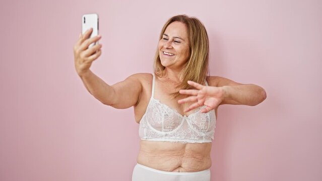 Middle age hispanic woman wearing lingerie having video call over isolated pink background