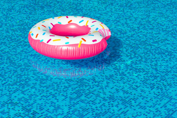 A rubber bitten donut with caramel sprinkles floats in a clean pool