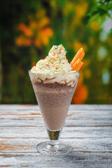 Chocolate milkshake with whipped cream decoration isolated on wood table. Tropical background.