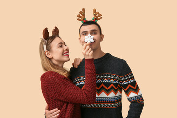 Beautiful young couple in reindeer horns with decorative snowflake on beige background